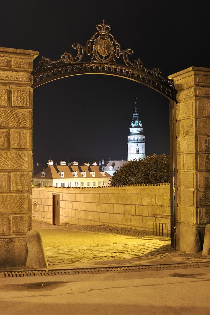 Kovaná brána s erbem, v pozadí zámecká věž